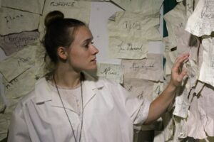 The Stranger: image of woman with hand on wall, surrounded by papers with names written on them. 